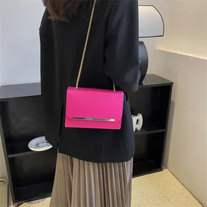 Sac bandoulière carré rose vif avec chaîne dorée porté par un mannequin en veste noire