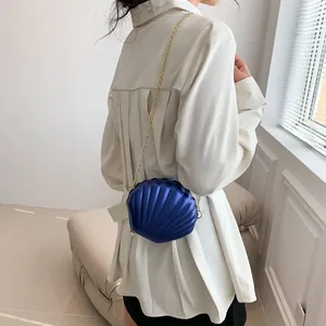 Blue shell-shaped crossbody bag with gold chain and pearl charm detail shown on model