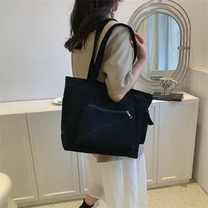 Détail du sac cabas noir en velours côtelé montrant la texture et la poche zippée avant