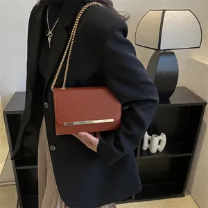 Détail du sac bandoulière en cuir rouge brique avec bordure dorée et chaîne