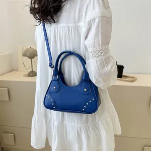 Borsa a mano blu a mezzaluna in pelle con borchie dorate indossata da una modella