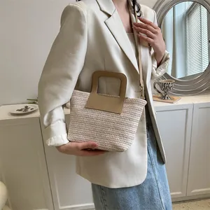Mannequin portant un sac seau en paille tissée crème avec poignées en cuir brun
