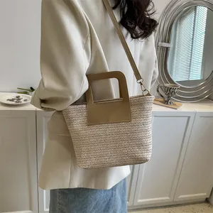 Détail du sac seau en paille tissée avec poignée en cuir marron et sangle dorée chic