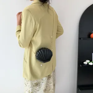 Detail of black shell-shaped crossbody bag with pearl pendant and gold chain strap