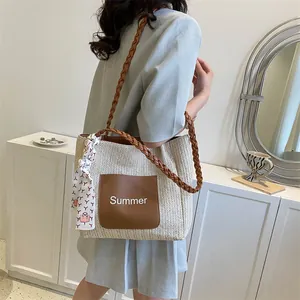 Detail of straw tote bag with brown leather pocket and summer lettering embroidery