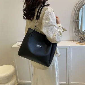 Detail of black leather tote bag featuring a white logo patch and chain-linked shoulder strap
