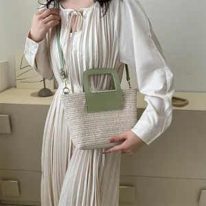 Détail du sac seau en paille tissée avec bandoulière en cuir vert porté par un mannequin