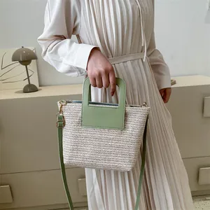 Détail d'un sac seau en paille tressée avec anse en similicuir vert et doré