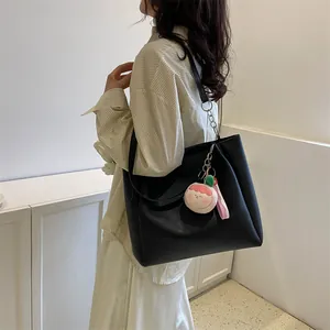 Detail of black leather tote bag with cute pink peach plush charm worn by model