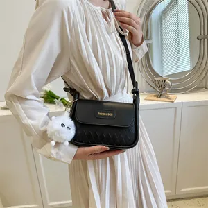 Detail of black crossbody bag with woven texture, golden tag, and white plush charm accessory