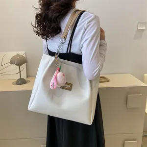 Detail of cream tote bag featuring light brown leather straps and metal chain accents