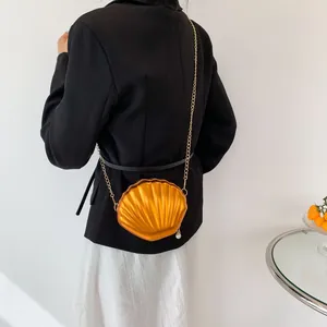 Detail of vibrant orange shell-shaped crossbody bag with gold chain and pearl zipper pull