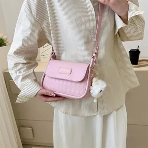 Pink quilted crossbody bag with plush pompom on a model wearing striped shirt