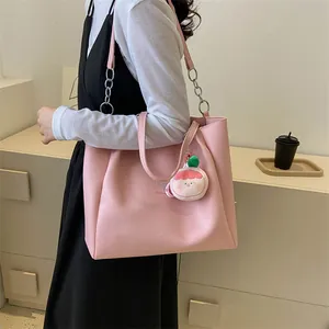 Detail of pink faux leather tote bag with metal chain strap and peach plush pendant
