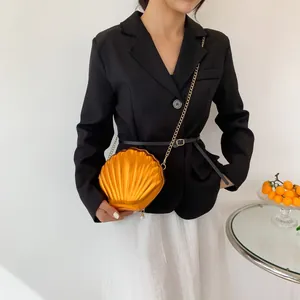 Detail of a golden shell-shaped chain bag featuring a metallic pleated texture and pearl charm