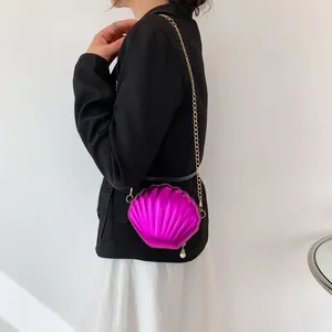 Detail of shell-shaped crossbody bag in magenta with gold chain and pearl pendant