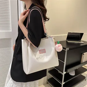 Close-up of white tote bag with pink leather label and peach plush charm on side