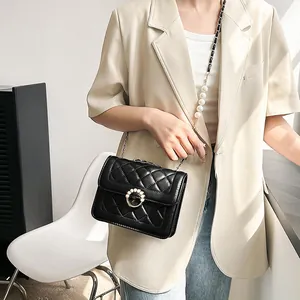 Detail of black quilted crossbody bag with pearl buckle and metal chain strap