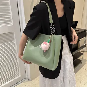 Detail of light green leather tote bag with gold chain strap and pink peach plush charm