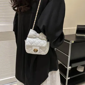 Close-up of white quilted crossbody bag with bow detail and gold chain strap
