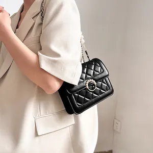 Detail of black quilted leather shoulder bag with pearl clasp and chain strap on a model