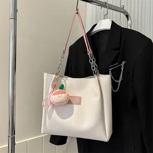 Detail view of white tote bag with pink leather label and peach plush charm on clothes hanger