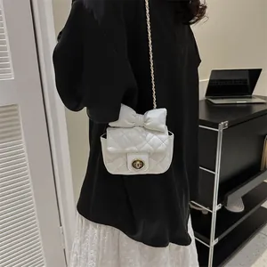 Detail of white quilted mini bag with bow accent, gold lock and chain strap