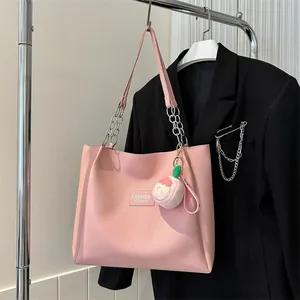 Close-up of pink leather tote bag with chain strap and peach plush charm on a blazer