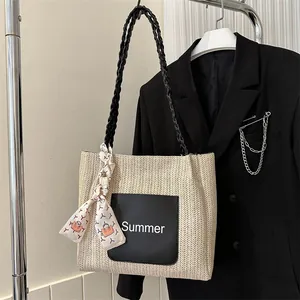 Close-up of beige woven tote bag with black straps and Summer patch detail