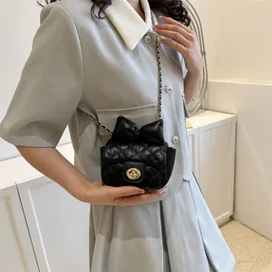 Detail of black quilted leather crossbody bag with bow and golden chain strap