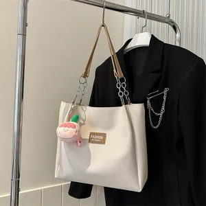 Detail of cream leather tote bag featuring silver chain straps and a pink peach charm