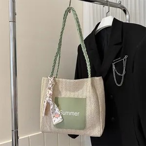 Detail of a beige straw tote bag featuring a green leather pocket and floral scarf handle