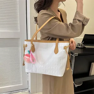 Détail d'un grand sac cabas blanc tissé avec poignées marron et pendentif en peluche rose