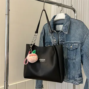 Detail of black leather tote bag with chain strap and cute peach plush charm detail