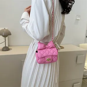 Pink quilted crossbody bag with large bow and gold chain strap worn by a model