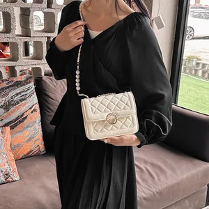 Close-up of white quilted crossbody bag with gold buckle and pearl chain strap