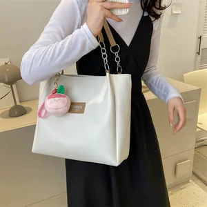 White faux leather tote bag with metal chain straps and pink peach charm detail