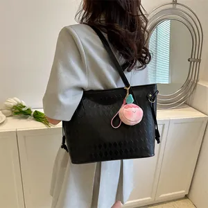 Détail d'un sac cabas noir matelassé avec un charme de pêche rose et une fine bandoulière