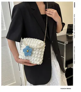 Detail of white bubble textured shoulder bag with pearl handle and blue flower charm
