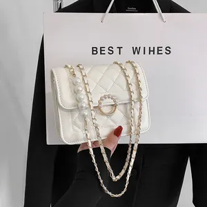 Close-up of white quilted crossbody bag featuring a pearl buckle and hanging pearl charm