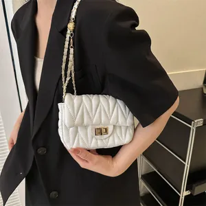 Close-up of white quilted leather crossbody bag with gold chain strap on a black blazer