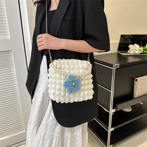 Detail of white pleated bubble crossbody bag with pearl strap and blue flower charm