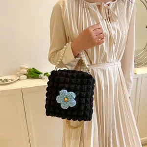 Detail of black pleated bubble bag featuring pearl handle and blue plush flower charm