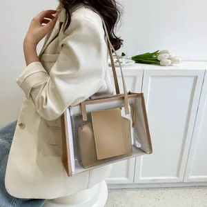 Close-up of a clear PVC tote bag with beige trim and matching inner pouch on a model