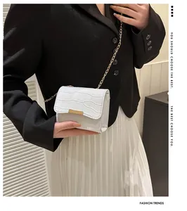 Close-up of white croc-effect crossbody bag with gold buckle and chain strap on model