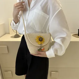 Detail of woven straw bucket bag featuring a sunflower accent and colorful pom-pom charms