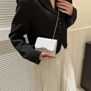 White faux crocodile leather crossbody bag with a gold chain strap worn by a model