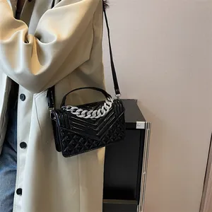 Détail du petit sac carré noir brillant avec chaîne argentée et texture matelassée