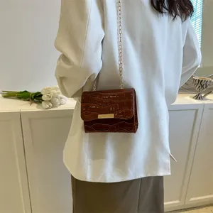 Close-up of dark brown crocodile-embossed flap bag with gold chain and metal clasp