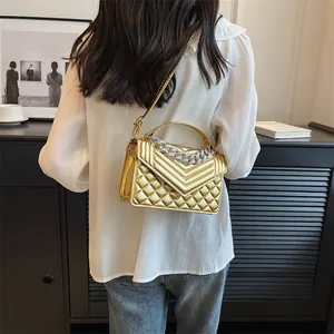 Détail d'un sac bandoulière matelassé doré avec une chaîne argentée et une bandoulière